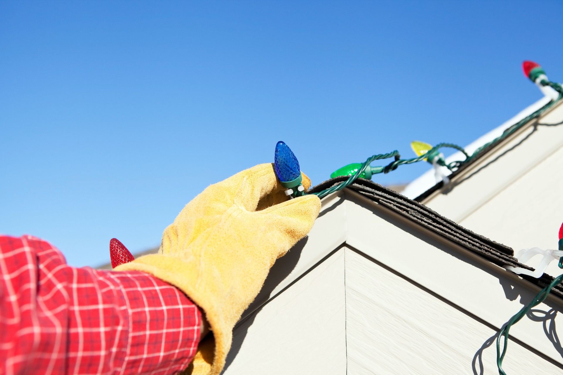 Hand Installing LED Christmas Lights on House Roof